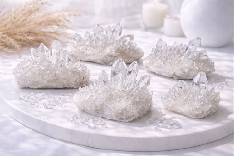 Multiple clear quartz crystal clusters arranged on a bright white surface in soft natural light, highlighting raw crystal points and natural clarity